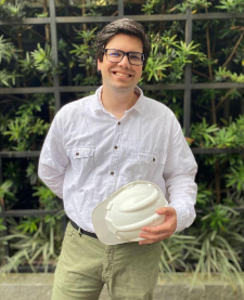 Engenheiro civil Eduardo sorrindo, segurando capacete de proteção branco em canteiro de obras da Stelblanc Engenharia Civil em Curitiba.